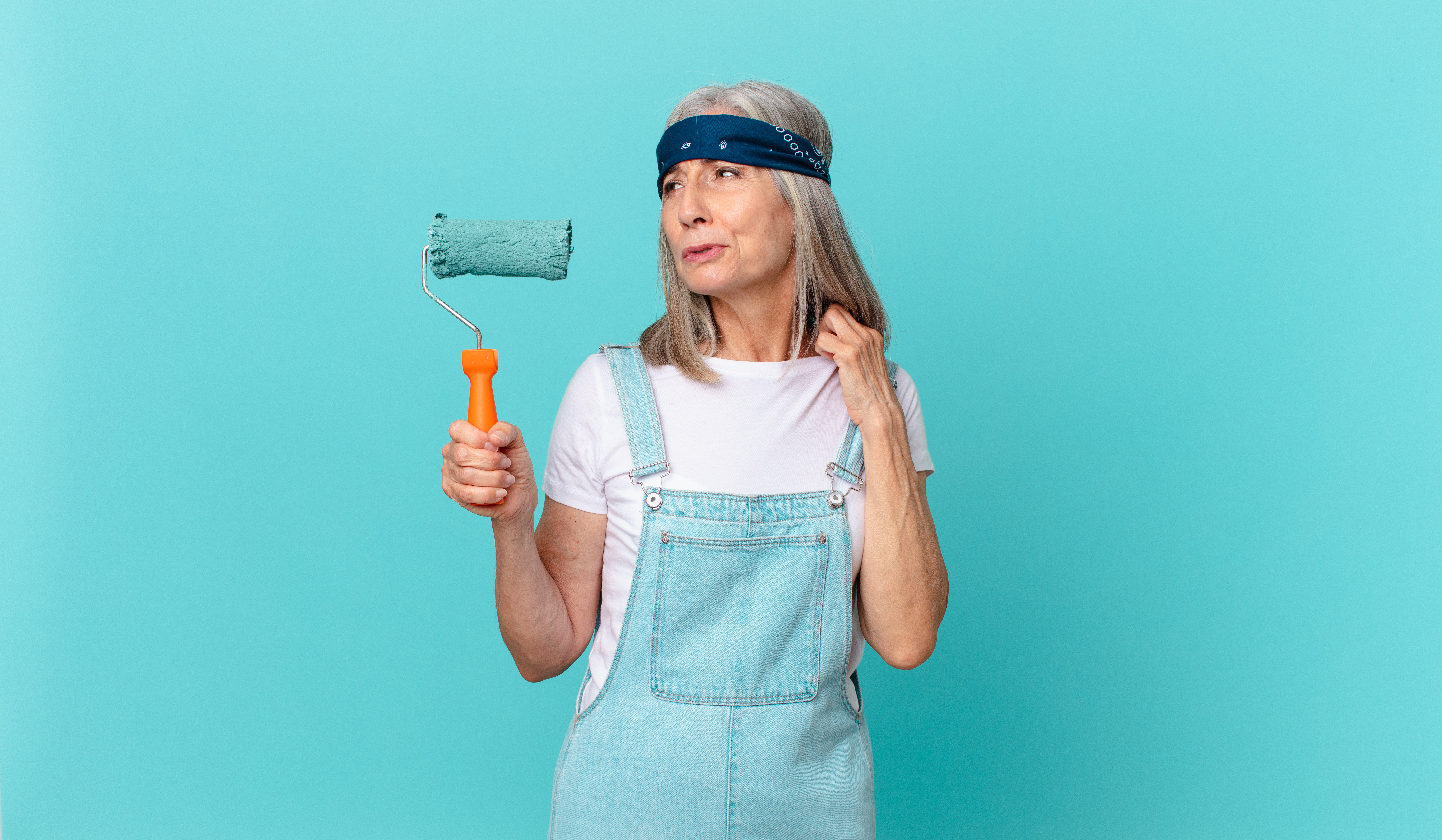 A woman holds a paint roller on a blue background.